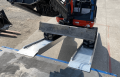 Digger driving up pair of loading ramps onto flat bed vehicle 