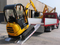 Mini digger driving up loading ramps 