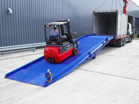 Forklift driving up mobile yard ramp into shipping container 