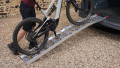 Single aluminium lightweight motorcycle ramp resting on the boot of a vehicle with a black push bike being pushed up