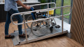 A wheelchair being pushed up a wheelchair ramp with handrails