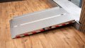 extra wide folding wheelchair ramp with red safety stripes, resting on a step ready for wheelchair loading