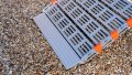 A rollable ramp resting the boot of a car - close up image of the foot end of the ramp on a gravel floor