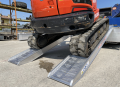 Digger driving up pair of loading ramps side view 