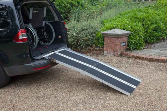 Multifold mobility scooter loading ramp resting on a car boot with a wheelchair stored in car