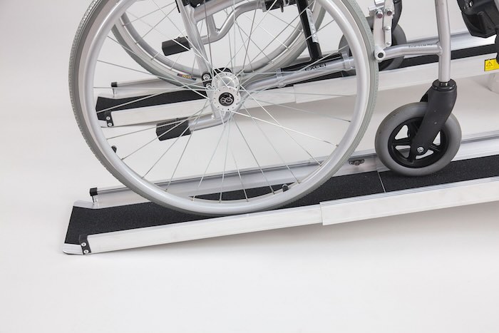 Pair of telescopic wheelchair ramps with black anti-slip surface, wheelchair going up the ramps