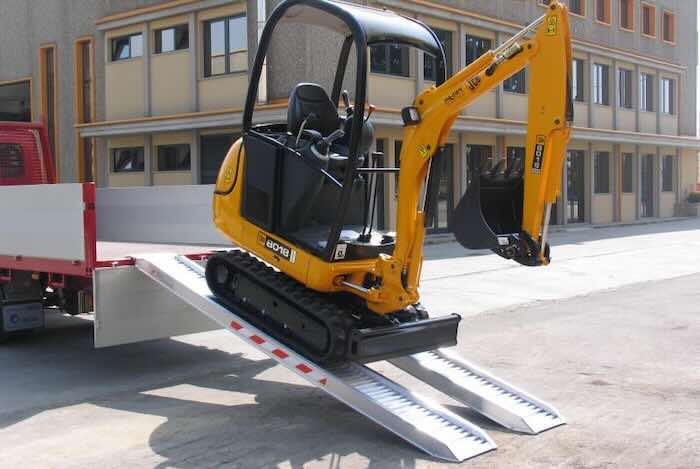 Rubber tracked machine driving up pair of aluminium loading ramps Rubber tracked machine driving up pair of aluminium loading ramps into flat bed vehicle