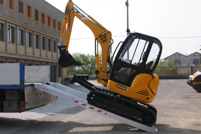 Rubber tracked machine driving up pair of aluminium loading ramps Rubber tracked machine driving up pair of aluminium loading ramps