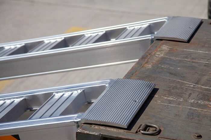 Rubber tracked machine driving up pair of aluminium loading ramps Rubber tracked machine driving up pair of aluminium loading ramps into flat bed vehicle
