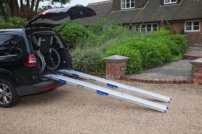 Pair of wheelchair ramps loading wheelchair into car boot 